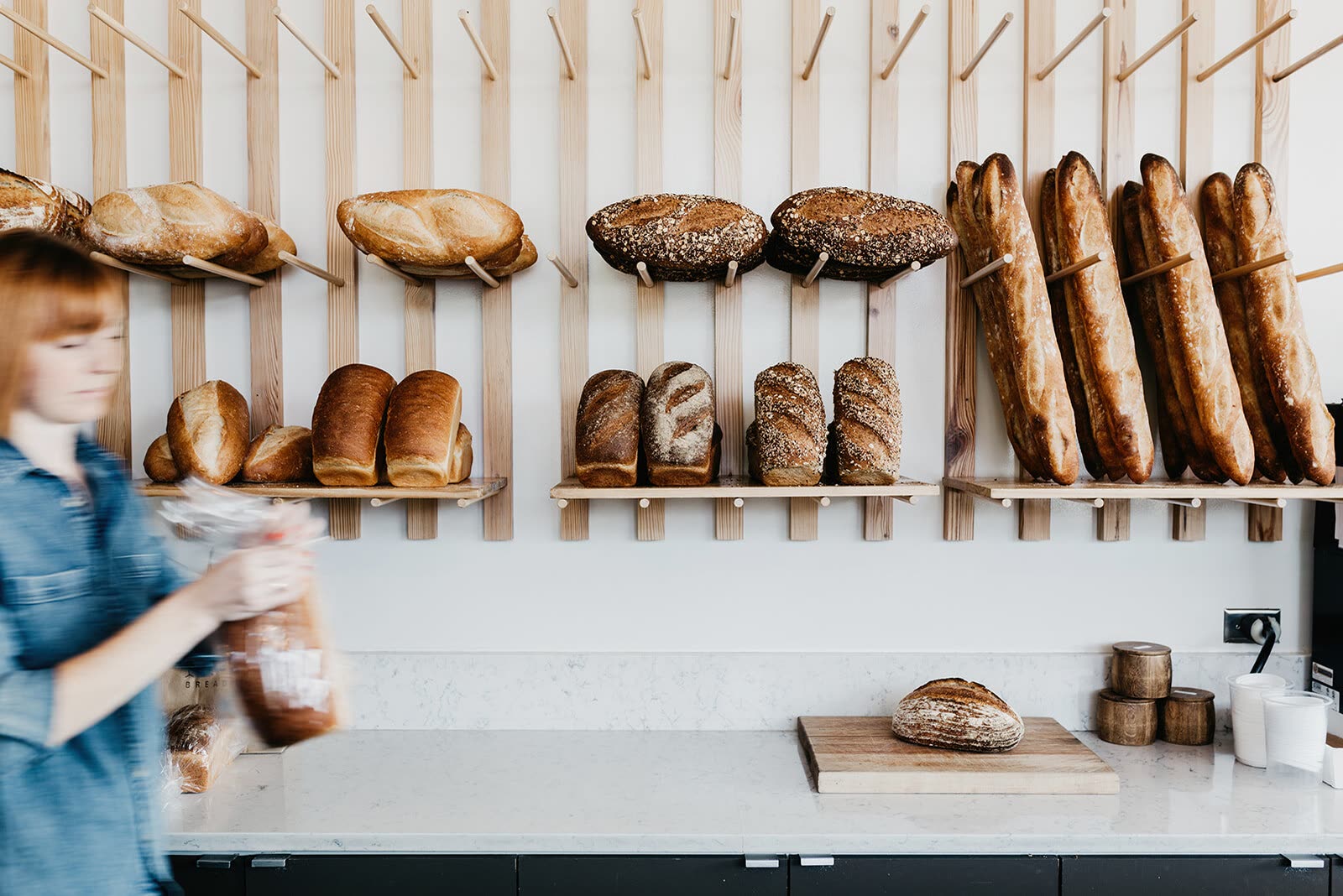 Loaves of sourdough, baguettes and sandwich bread on wall-mounted wooden racks above the counter at Yellow Dog Bread Co.